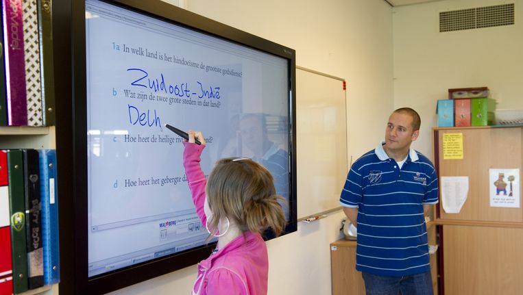 Een leerling schrijft op een digitaal schoolbord. Leraar kijkt toe. Beeld anp