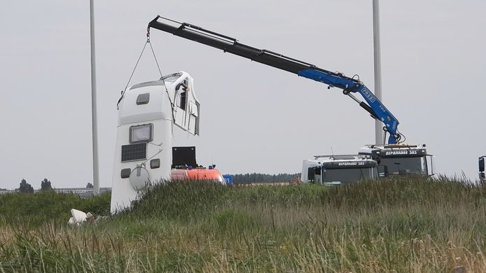 Een takeldienst hijst met een kraan een deel van de camper uit de gracht naast de E40 in Zandvoorde.