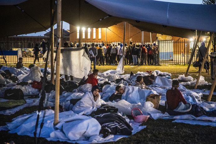 Asielzoekers bij het aanmeldcentrum maken zich onder luifeltenten op voor de nacht in de buitenlucht.