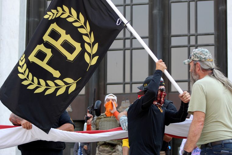Een activist zwaait de vlag van de Proud Boys, een rechtse groep, voor het parlementsgebouw van de Amerikaanse staat Oregon. Trump zei over hen: ‘Stand back and stand by’ – ‘Stop nu, maar blijf paraat’.  Beeld AP