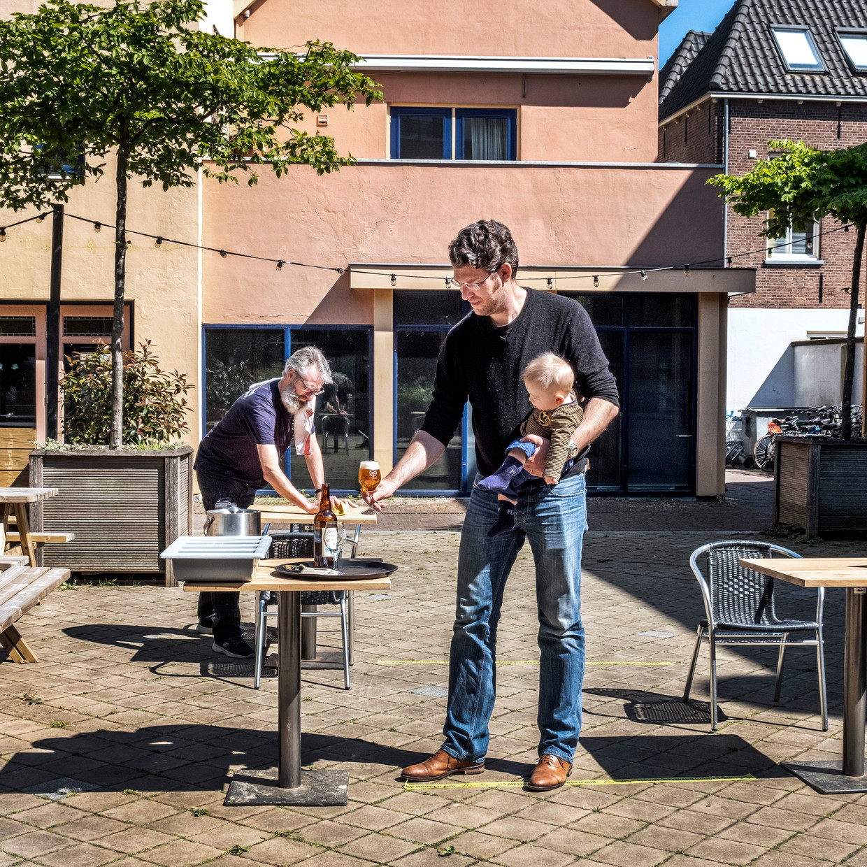 Stefan Duurkoop (met baby), de eigenaar van de stadsbrouwerij Wageningen, bekijkt hoe de anderhalvemeterregels uitpakken op zijn terras. Beeld Raymond Rutting / de Volkskrant