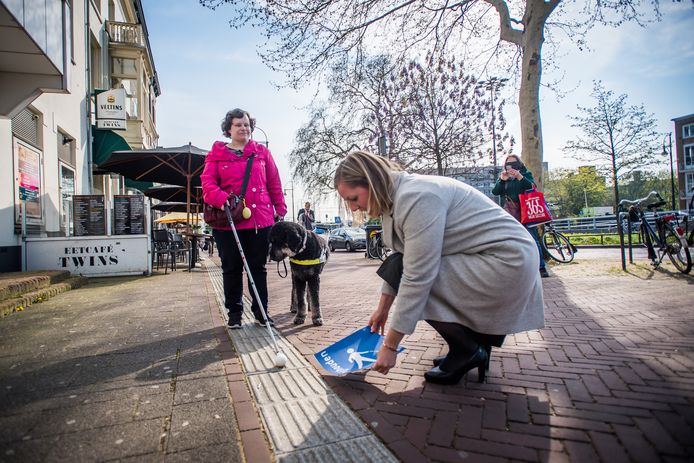 Martien Louwers plakt in aanwezigheid van Marjolein van den Broek en haar hond Harvey een sticker naast de geleidelijn. Foto: Rolf Hensel.