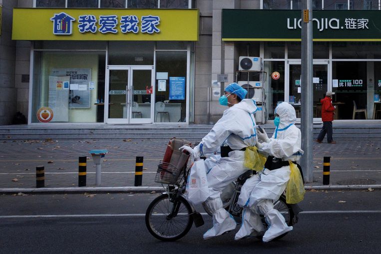  Zorgmedewerkers op een elektrische fiets door Peking. Ook in de hoofdstad namen de zerocovidrestricties toe.  Beeld REUTERS