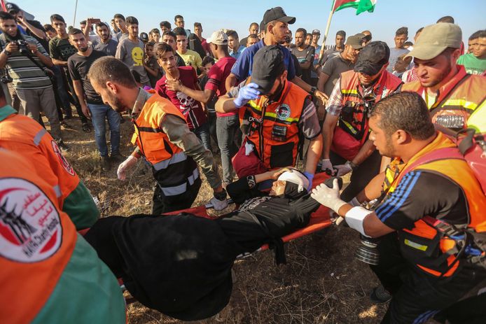Palestijnse hulpverleners dragen een gewonde demonstrant weg aan de grens met Israël in Gaza.
