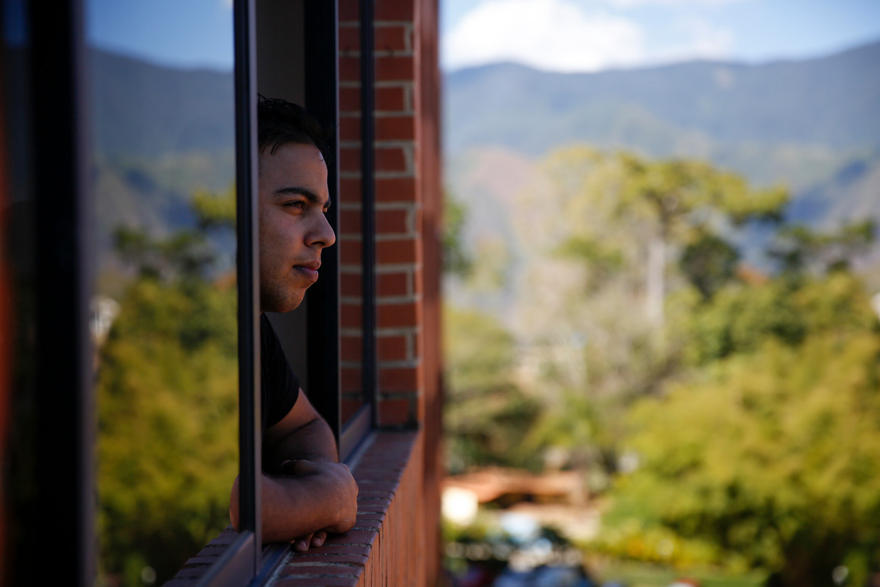 Hassan Al Ankouchi kijkend uit zijn raam in Caracas. Beeld Marco Bello