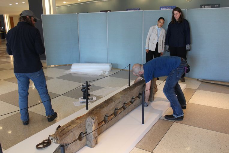 Medewerkers van het Rijksmuseum rond de houten voetboei, waarin meerdere mensen tegelijk konden worden vastgeketend, tijdens het opbouwen van de tentoonstelling in het VN-gebouw in New York. Beeld Karlijn van Houwelingen