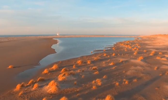 De laaghangende zon geeft de Zandmotor een gouden gloed.