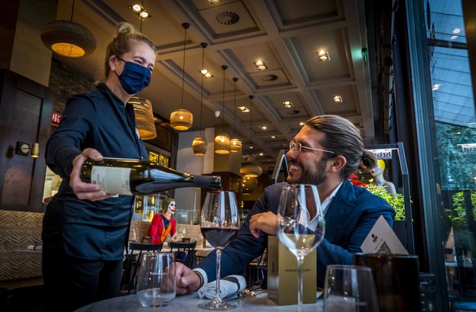 Een ober in een restaurant in Amsterdam draagt een mondmasker. Dat is daar nu ook verplicht.