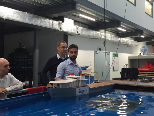 Onderzoekers van de TU Delft leggen hun zelfvarende modelschip in het water van één van de bassins van de Faculteit Werktuigbouwkunde. Links Rudy Negenborn, achteraan Milinko Godjevac