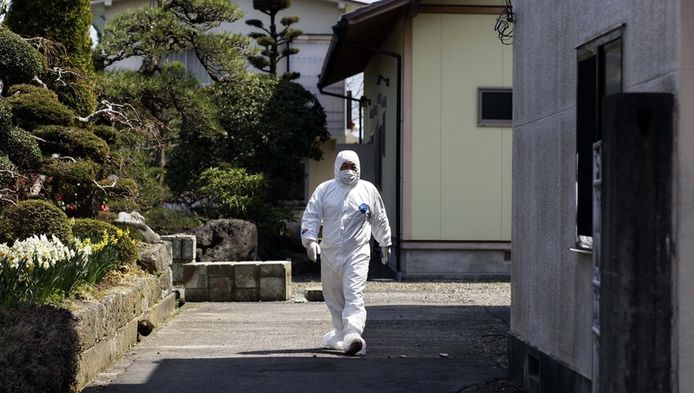 Een man in beschermende kleding loopt door het verlaten plaatsje Futaba