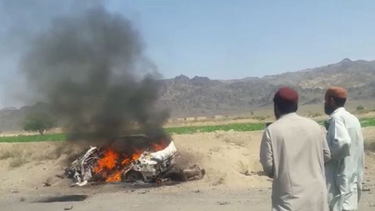 Pakistanen kijken naar het brandende wrak van de auto die met drones is aangevallen. In de wagen zouden een chauffeur en de leider van de Afghaanse Taliban hebben gezeten. Beeld epa