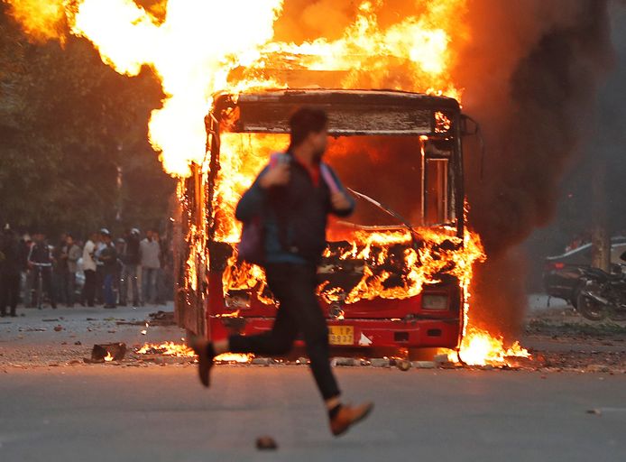 Een man rent voor een uitbrandende bus langs in New Delhi, waar rellen plaatsvonden tegen een nieuwe burgerschapswet die