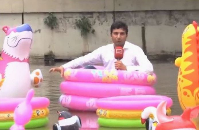 De reporter doet verslag van het overstroomde Lahore vanuit een roze kinderzwembadje, omringd door kinderspeelgoed.