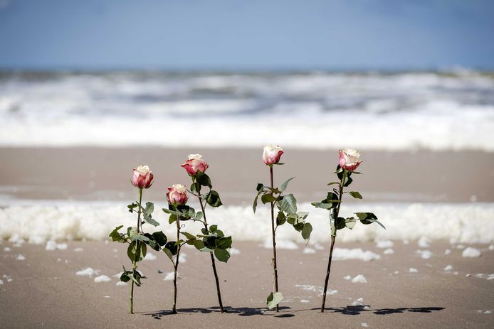 Bloemen tussen het schuim op het strand van Scheveningen. De badplaats is in rouw. Slecht weer heeft vijf surfers het leven gekost.