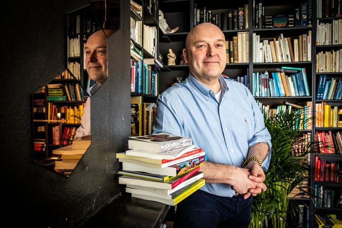 Veelschrijver, linguïst en communicatiedeskundige Bart Bruijnen met de stapel boeken van zijn hand voor zijn boekenkast.