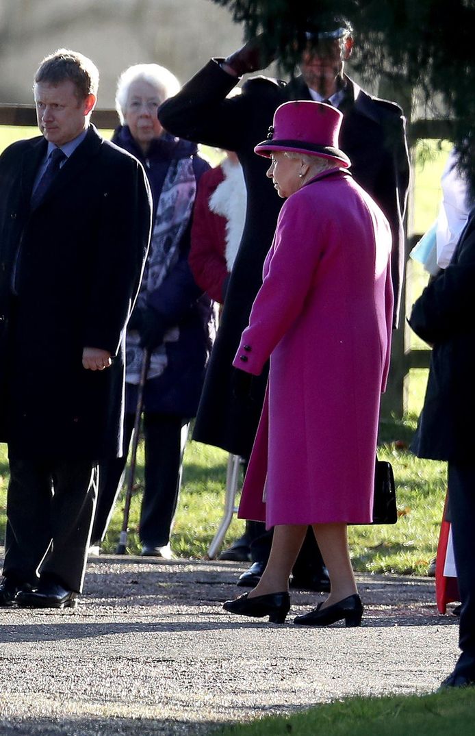Queen Elizabeth II in een lange overjas, zwarte leren schoenen en een hoed.