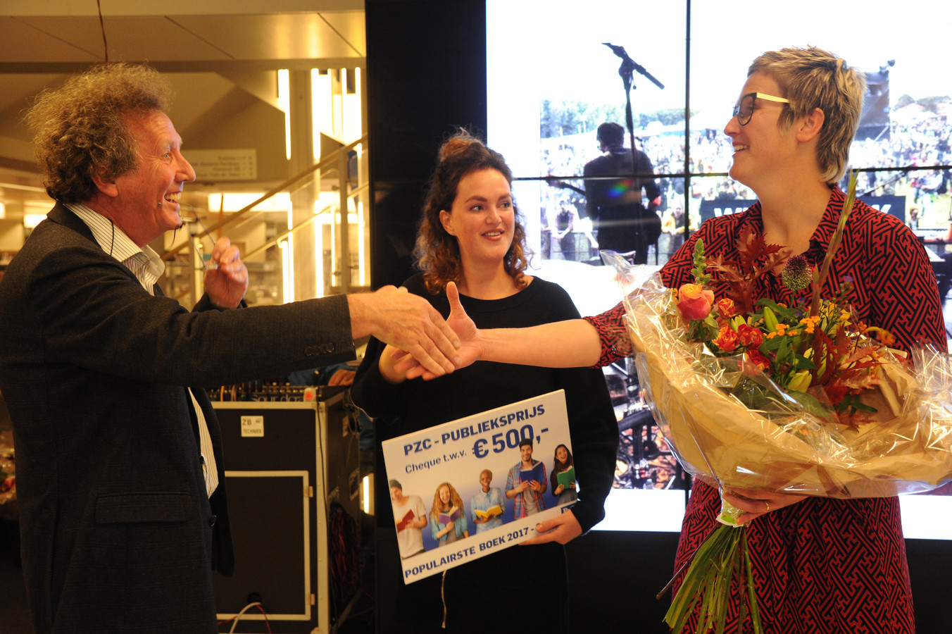 PZC-journalist Jan van Damme overhandigt de PZC-Publieksprijs aan Karlijn de Splenter (midden). Vormgeefster Corinne Lecluyse neemt de bloemen in ontvangst. Het jubileumboek Weitjerock kreeg de meeste stemmen: 368.