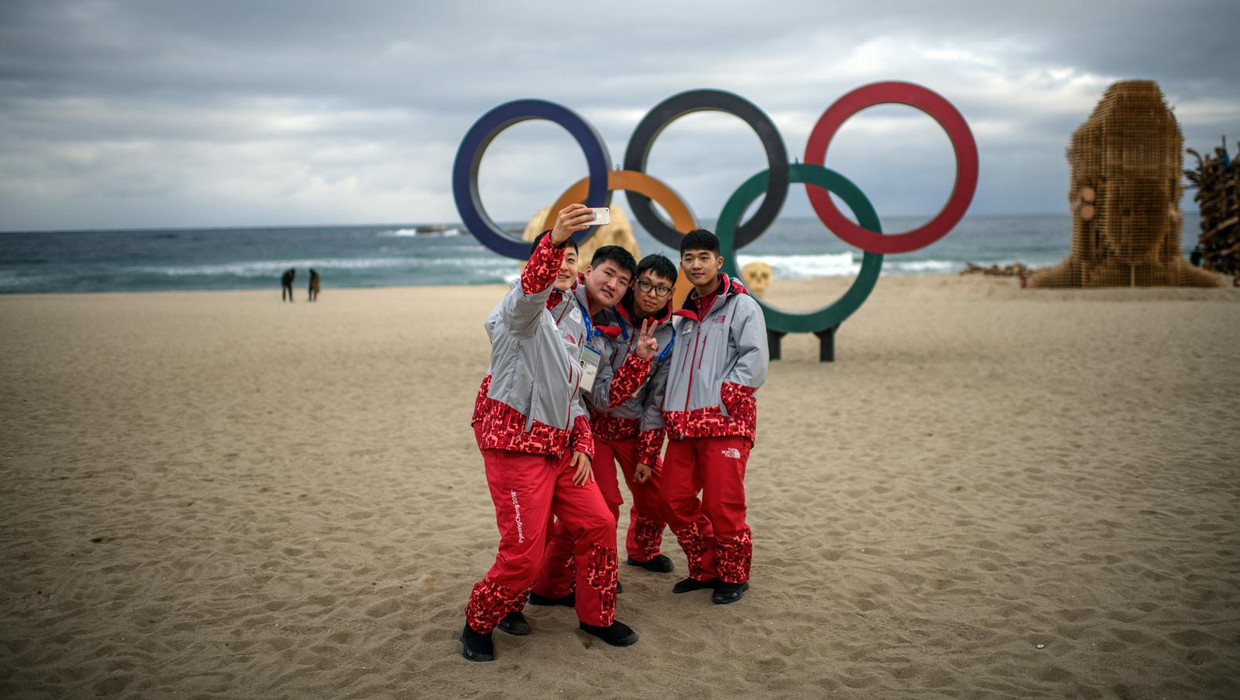 Vier jongemannen die als vrijwilligers meehelpen bij de organisatie van de Winterspelen in Zuid-Korea maken een selfie bij de Olympische ringen op het strand van Gangneung. Beeld getty