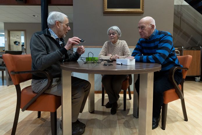 Vrijwilliger Welzijn Meierij lost bij senioren via de ‘knoppendienst’ storingen op aan apparaten. Vrijwilliger Peter Termeer (links) legt aan Elly en Toon Witlox uit hoe een tv-streamer zorgt dat mensen met een hoorapparaat ontspannen televisiekijken.
