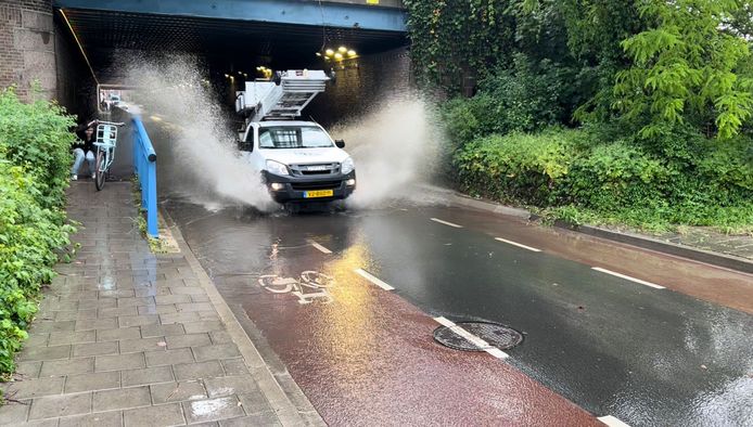 Beeld van het moment in Deventer waarop een meisje nog net achter haar fiets kan schuilen voor een plens water die op haar afkomt.