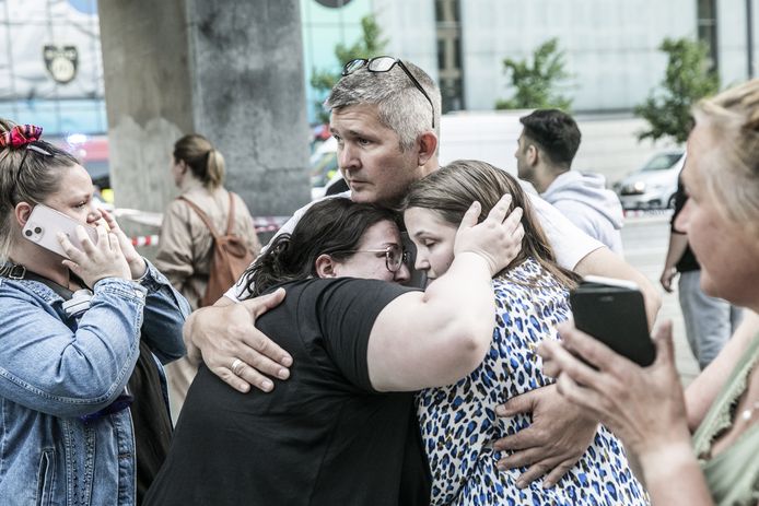 Drie mensen omhelzen elkaar voor het winkelcentrum waar de schietpartij plaatsvond.