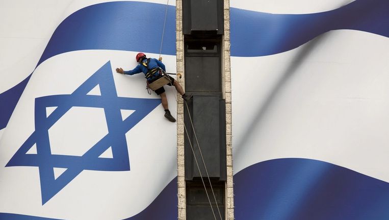 Een man hangt plakt een billboard van de Israëlische vlag ter gelegenheid van Israëls 65-jarige bestaan. Beeld epa
