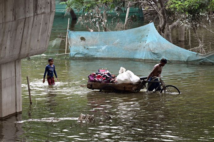 Beeld ter illustratie. Een man duwt een fietskar geladen met zijn bezittingen in een overstroomd laaggelegen gebied nadat de Yamuna-rivier overstroomde als gevolg van moessonregens, in New Delhi.