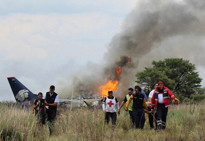 Reddingswerkers dragen een gewonde persoon weg van het brandende vliegtuig.