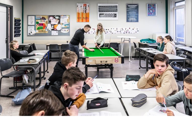 Wiskundeleraar Ruben Knippenbergh, achterin, legt een leerling uit hoe ze de bal in een rechte lijn kan stoten.  Op de voorgrond zit het groepje dat theorieles krijgt.  Beeld Roger Dohmen Fotografie