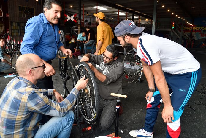 Salim (blauw overhemd) grijpt in bij de fiets van Saïd (grijze hoodie). Vrijwilliger Rik en tolk Samer helpen.