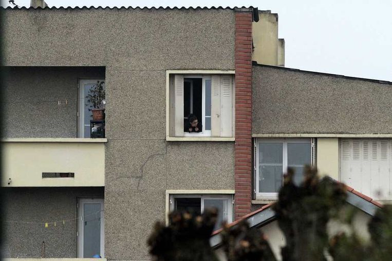 Een buurtbewoner kijkt uit het raam naar de belegering. Beeld reuters