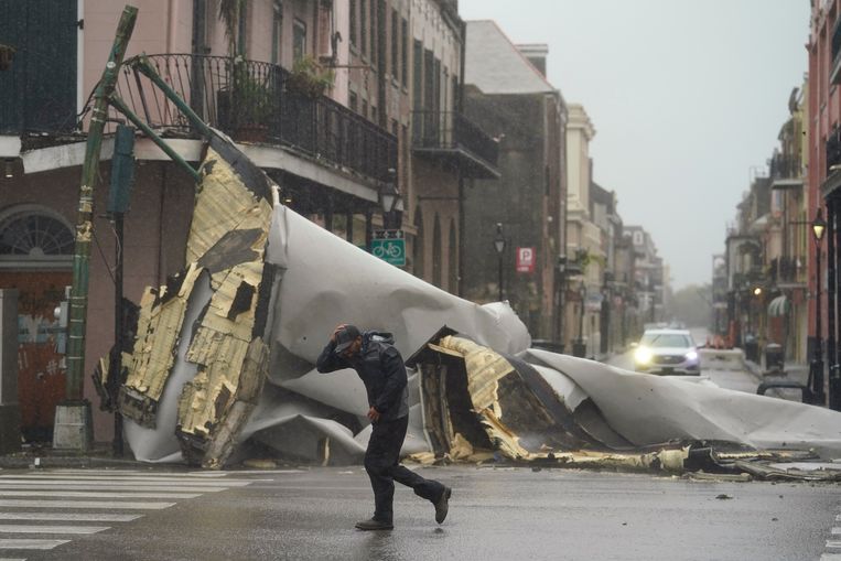 Een man loopt langs een stuk dak dat van een gebouw is gewaaid in de French Quarter in New Orleans Beeld AP