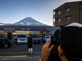 Een toerist poseert voor een supermarkt, met Mount Fuji op de achtergrond. Het is een populaire plek voor foto's.