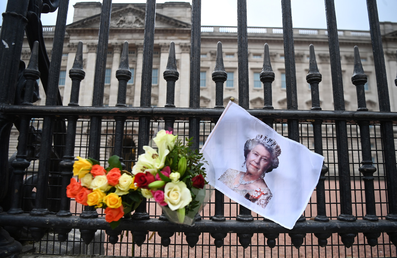 Een foto van de Britse koningin Elizabeth en bloemen aan het hek bij Buckingham Palace.