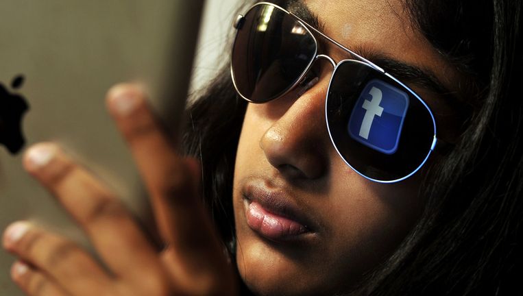 Het logo van Facebook reflecteert in de zonnebril van een vrouw die browst op een iPad Beeld ANP