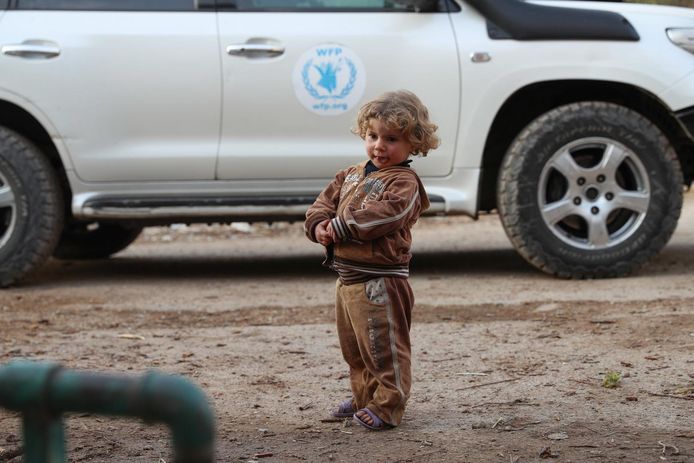 Een kindje staat naast een wagen van de Verenigde Naties in de buurt van Damascus.