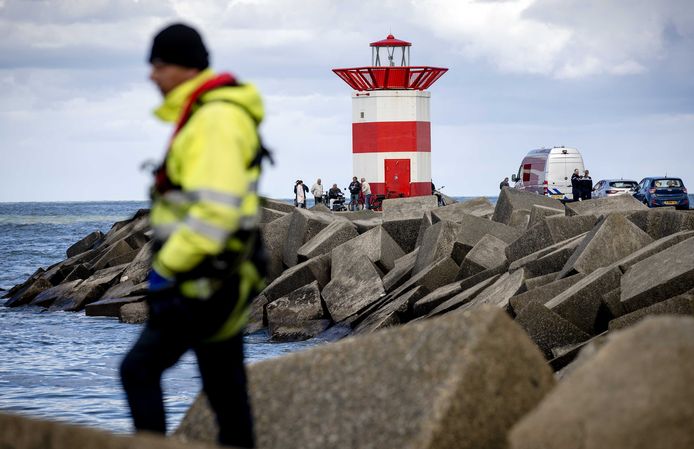 Een medewerker van de Koninklijke Nederlandse Redding Maatschappij zoekt op het Noordelijk Havenhoofd Scheveningen mee naar het lichaam.