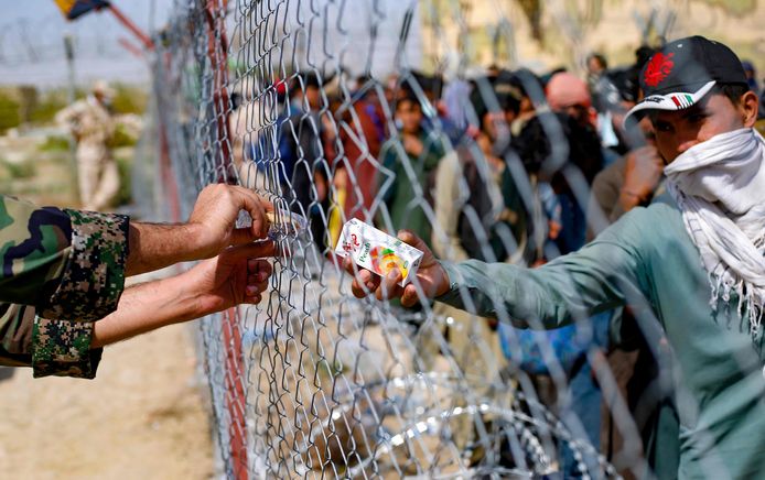 Een Iraanse soldaat steekt Afghaanse vluchtelingen wat eten en drinken toe door een hek aan de Afghaans-Iraanse grens.