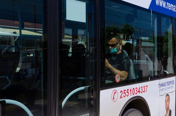 Een busreiziger met (een verkeerd gedragen) mondmasker op een bus in de Griekse hoofdstad Athene. Het gebruik van airco op het Griekse openbare vervoer is tot nader order niet toegelaten.