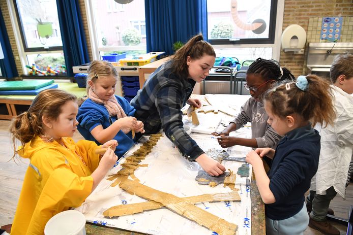 Anouk Akkerman van CV Oké helpt de kinderen op De Hoge Waai met de lijm en het papier dat geplakt moet worden tijdens de lessen die Stichting Raamsdonkse Karnaval (SRK) deze weken geeft over het bouwen van carnavalswagens.