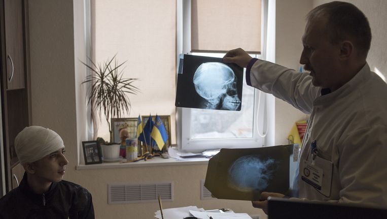 Chirurg Joeri Skrebets toont Sasja Gristisjenko een röntgenfoto van diens schedel. Een deel daarvan is vervangen door plastic en titanium. Beeld Yuri Kozyrev/ Noor
