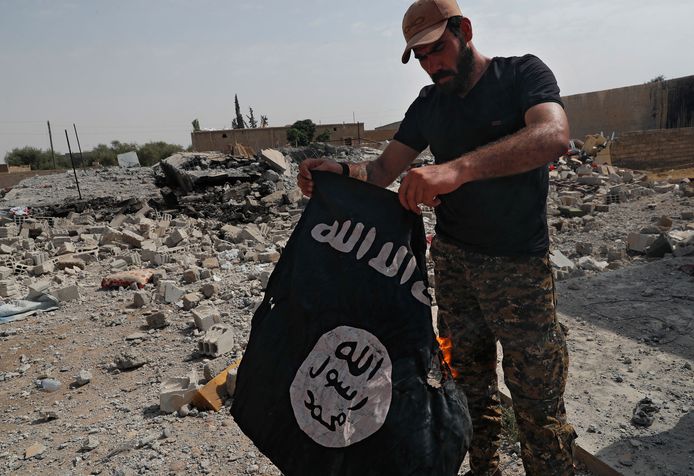 Een strijder van een christelijke Syrische militie die strijdt tegen IS mat een vlag van de terreurorganisatie.