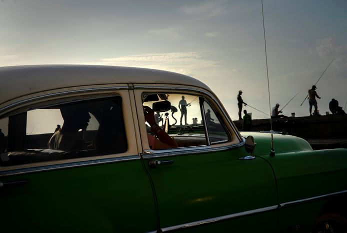 Een auto rijdt langs vissers in Havana.