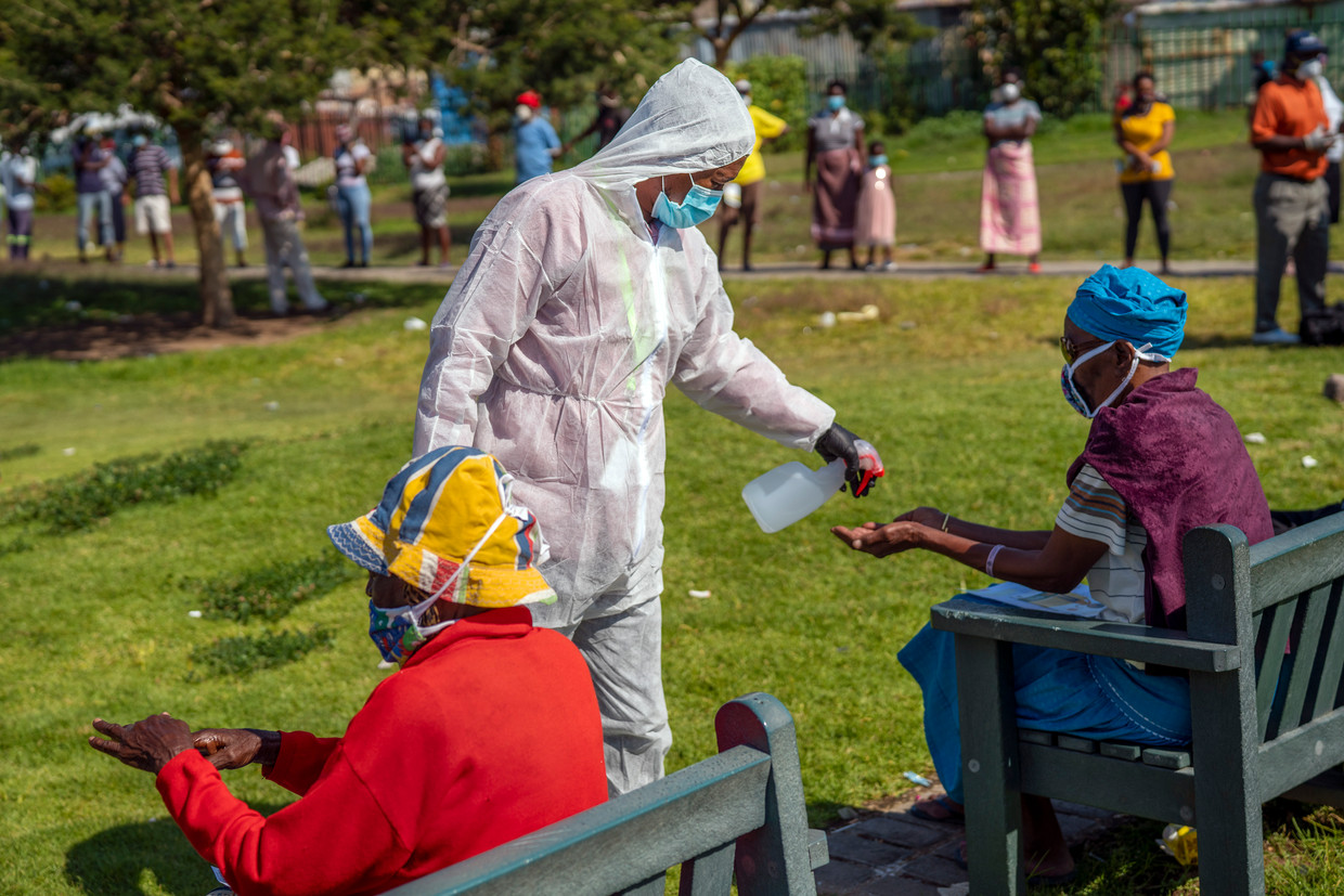 Op een testlocatie in het township Diepsloot, waar inwoners op het coronavirus worden getest, krijgen mensen desinfecterende spray op hun handen gespoten. Veel inwoners willen niet worden getest.