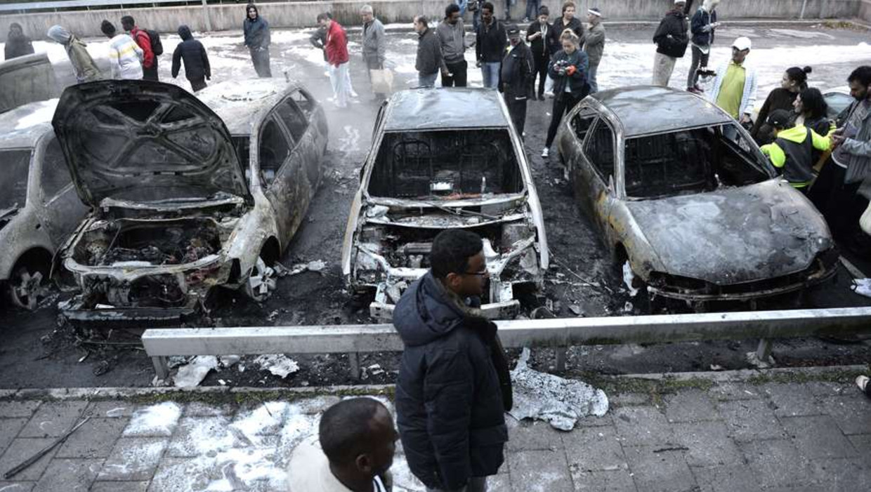 Mensen inspecteren de in brand gestroken auto's in Stockholm. Beeld afp