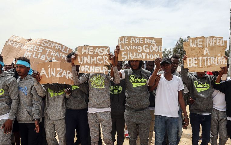 Migranten die gestrand zijn in Libië houden kartonnen protestborden omhoog bij een bezoek van de secretaris-generaal van de Verenigde Naties Antonio Guterres in het kamp bij Tripoli.  Beeld AFP