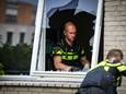 Collega’s van de gewond geraakte agent ruimen de glasscherven van het ingeslagen raam op.