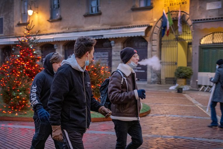 Jongeren met het mondmasker naar beneden getrokken lopen in de oude stad van Bergamo in kerstsfeer. Beeld Patrick Post