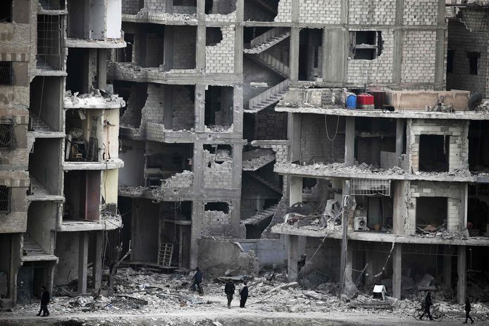 Syriërs lopen tussen verwoeste gebouwen in de door rebellen bezette streek Ghouta.