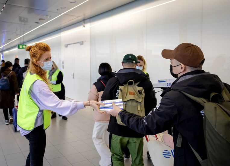 Een medewerker van de GGD deelt op Schiphol gratis coronazelftesten uit onder reizigers uit China.  Beeld ANP, Robin van Lonkhuijsen